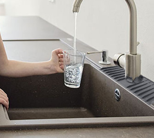 Filling a glass at a kitchen sink fitted with the silicone faucet drip catcher tray