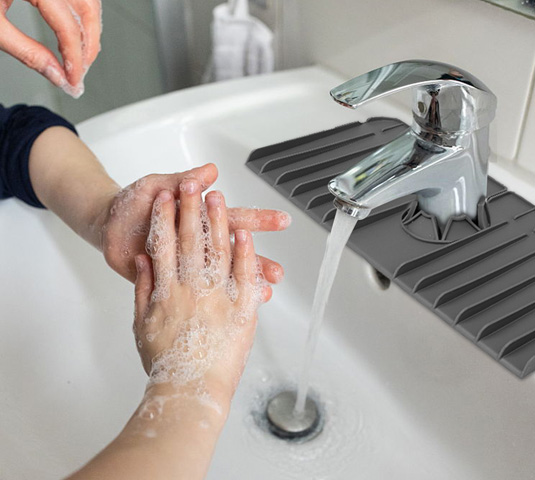 Washing hands at a bathroom sink fitted with the silicone faucet drip catcher tray